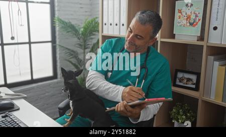 Hispanischer Mann mittleren Alters Tierarzt in einer Klinik mit zwei Chihuahuas, die Notizen auf einem Klemmbrett machen. Stockfoto