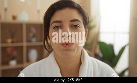 Eine junge Frau in einem Spa, die einen weißen Bademantel trägt und in einem ruhigen Schönheitszentrum ein Pouty-Gesicht macht Stockfoto