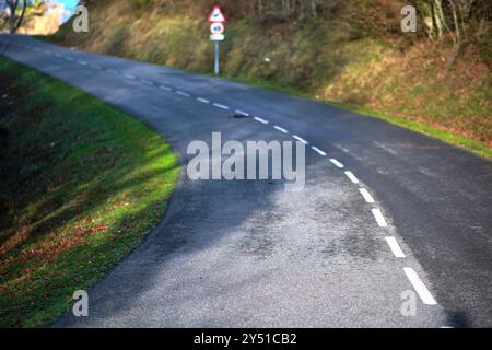 Eine kurvige Landstraße mit einem Straßenschild, umgeben von grasbewachsenen Hängen und Herbstlaub. Vitoriano, Araba, Baskenland, Spanien. Stockfoto