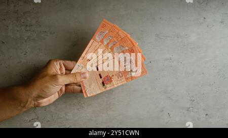 Halten Sie mehrere malaysische 10-Ringgit-Banknoten vor einem konkreten Hintergrund, zeigen Sie die lokale Währung und vermitteln Sie ein Gefühl für Finanzen und E Stockfoto