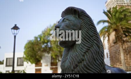 Löwenstatue in der Stadt teguise auf lanzarote mit Palmen, Straßenlaternen und historischen Gebäuden unter dem Sommerhimmel Stockfoto