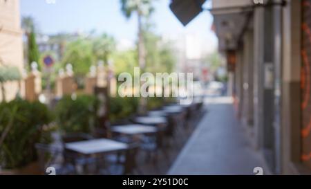 Unscharfer Hintergrund einer leeren Café-Terrasse mit Bokeh-Effekt, unscharfen Tischen und Stühlen, die an einem sonnigen Tag eine ruhige Straße säumen Stockfoto