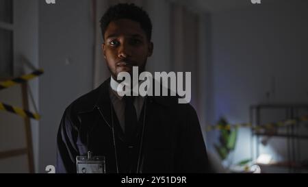 Ein afroamerikanischer Detective in Klage ermittelt den Tatort drinnen mit Warnband Stockfoto