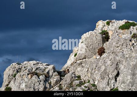 Eine Nahaufnahme einer zerklüfteten Felsformation mit grünen Flecken vor einem dramatischen, dunklen, bewölkten Himmel. Vitoriano, Araba, Baskenland, Spanien. Stockfoto