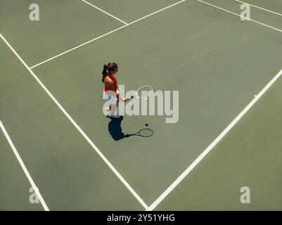 Luftaufnahme einer Frau, die sich an einem sonnigen Tag auf Tennis vorbereitet und einen leeren Platz mit viel Kopierraum zeigt. Stockfoto