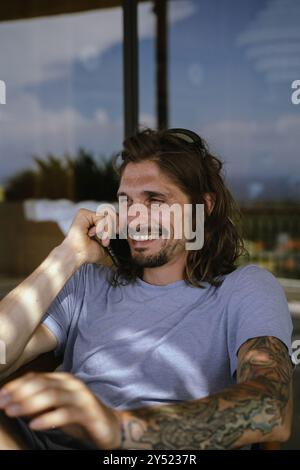 Mann, der auf dem Smartphone spricht, auf einem Stuhl sitzt. Stockfoto