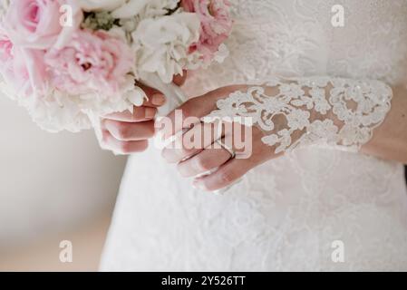 Die Hände der Braut halten einen rosa-weißen Blumenstrauß und zeigen Spitze und Ring. Stockfoto