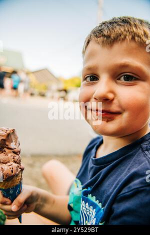 Ein kleiner Junge mit einem schokoladigen Lächeln, der eine Eiskugel hält Stockfoto