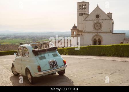 Ikonisches altes italienisches Auto „Fiat 500 Cabrio“, das vor der Kirche San Francesco (Basilika di San Francesco) in Assisi, Region Umbrien, Italien parkt Stockfoto