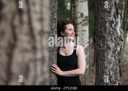 Glückliche junge Frau allein im Wald lehnt sich an den Baum Stockfoto