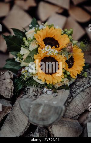 Hochzeitsstrauß mit Sonnenblumen und Ringen auf gestapeltem Holz, rustikale Einrichtung Stockfoto