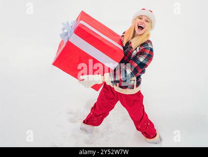 Weihnachtsfrau mit einem riesigen Geschenkkarton. Frohe Winterzeit. Hipster Girl mit Weihnachtsgeschenk auf Schnee Winterlandschaft. Weihnachten Winter Menschen. Stockfoto