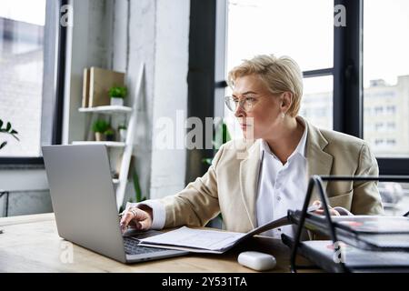 Eine elegante Frau, stilvoll gekleidet, konzentriert sich auf ihre Arbeit an einem modernen Schreibtisch in einem hellen Raum. Stockfoto