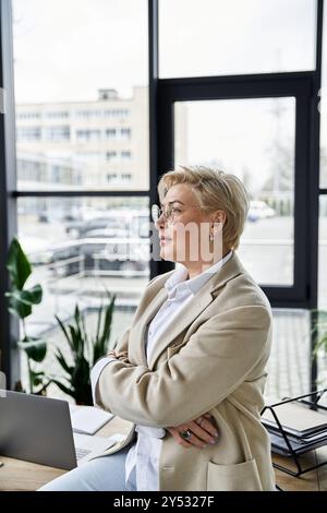 Eine Erwachsene Frau in schicker Kleidung steht selbstbewusst und denkt über ihren nächsten Zug in einem hellen Büro nach. Stockfoto