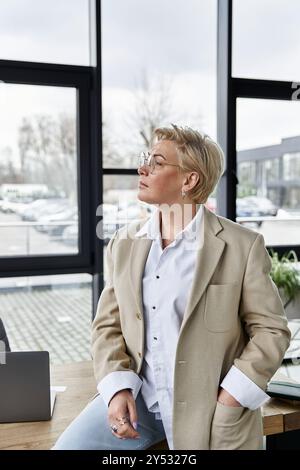 Die selbstbewusste Frau in raffinierter Kleidung genießt einen reflektierenden Moment in einem modernen Bürobereich. Stockfoto