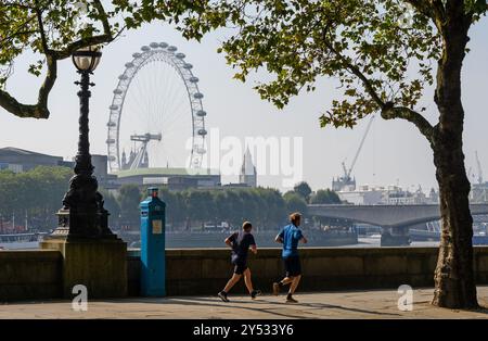 London, Großbritannien. Das London Eye vom Victoria Embankment auf der anderen Seite des Flusses aus gesehen. Zwei Männer laufen vorbei Stockfoto