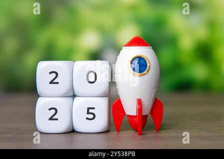 Eine Spielzeugrakete neben einem weißen Würfel mit der Nummer 2025. Unternehmensgründung, Zukunftsziele, Neuanfang-Konzept. Stockfoto