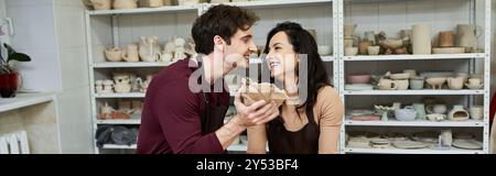 Ein Paar bastelt fröhlich Keramik und teilt einen zarten Moment in einem hellen Studio. Stockfoto