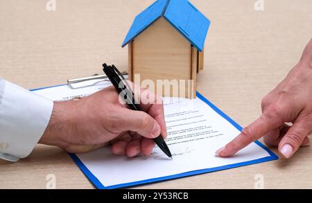 Hand des Maklers zeigt dem Kunden, wo der Hypothekenvertrag oder Mietvertrag unterzeichnet werden soll. Immobilienmakler und -Käufer unterzeichnen ein Kaufdokument Stockfoto