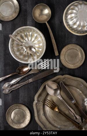 Vintage Zinnteller, Schüsseln und Besteck auf schwarzem Tafel Hintergrund. Flache Lagen. Draufsicht. Lebensmittelkonzept. Lebensmittelfotografie in dunkler Stimmung. Stockfoto