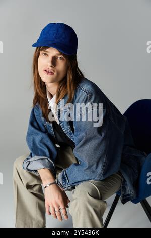 Ein modischer junger Mann mit langen Haaren sitzt lässig und zeigt seinen einzigartigen Stil und sein Selbstvertrauen. Stockfoto