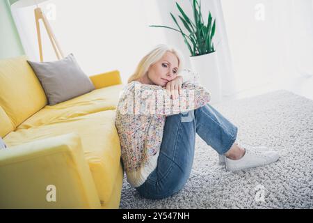 Porträt der netten alten Dame sitzen Boden schlechte Stimmung tragen Pullover Wohnzimmer Wohnung drinnen Stockfoto