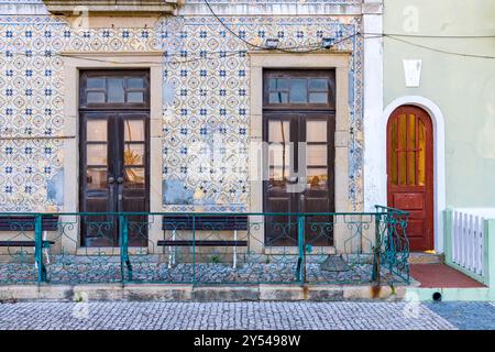 Ein Gebäude mit einer roten Tür und zwei alten Holzfenstern. Das Gebäude ist alt und hat eine geflieste Fassade Stockfoto