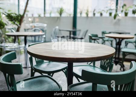 Mittlere Nahaufnahme eines runden Holztisches mit türkisfarbenen Stühlen im Café Stockfoto