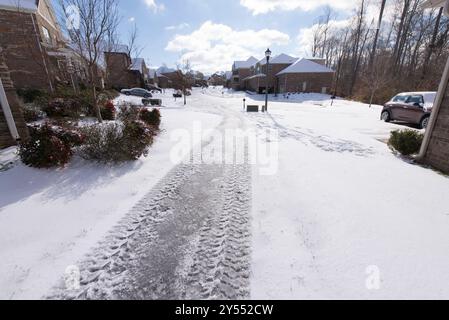 Ein ruhiges, schneebedecktes Vorstadtviertel mit Reifenspuren auf einer Einfahrt unter hellem, sonnigem Himmel. Stockfoto