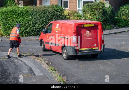Postbote in knallroter Uniform, der sich einem Postwagen nähert, der Briefe nach Hause in Großbritannien geliefert hat. Stockfoto