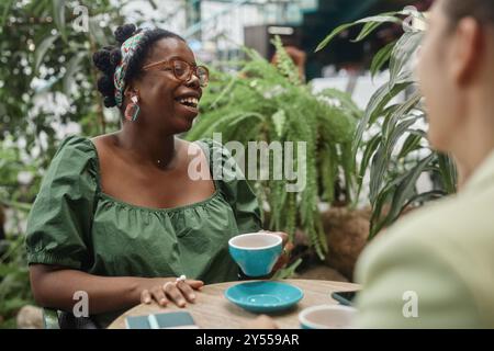 Zwei birassische Freunde verbringen Freizeit im Café, lustige afroamerikanische junge Frau lacht, während sie Freunden die Geschichte zuhört Stockfoto