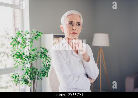 Positive schöne reife Dame Arzt Blick gemindert nachdenklich professionelle tragen weißen Labormantel Licht Krankenhaus Büro Stockfoto