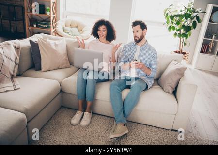 Foto von zwei Leuten Mädchen verblüfft aussehen Netbook-Anzeigen Guy sitzt Couch fühlt sich unglücklich in der Zimmerwohnung Stockfoto