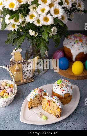 Zwei kleine Osterkulichs mit kandierten Früchten in weißer Glasur mit bunten Streuseln im Schnitt. Bemaltes Hühnchen und Wachteleier. Traditionelle Osterbak Stockfoto