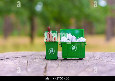 Grüner Miniaturbehälter mit Papierabfällen und Glasflaschen, wodurch die Umweltverantwortung durch Abfalltrennung gestärkt wird. Stockfoto