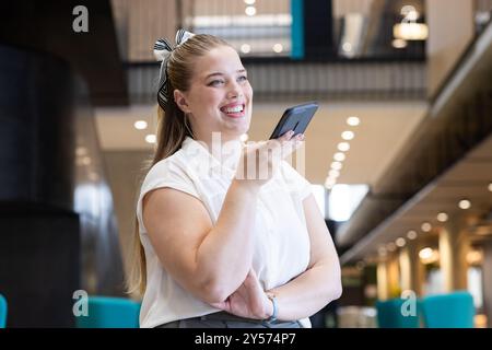 Smartphone in der Hand, lächelnde Geschäftsfrau, die Sprachnachrichten im modernen Büro aufnimmt Stockfoto