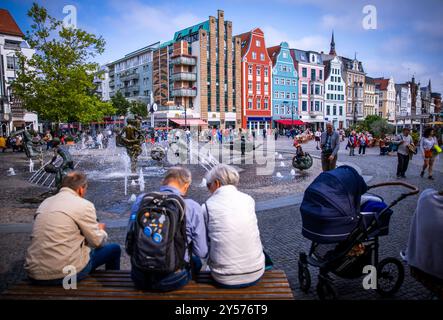 Rostock, Deutschland. September 2024. Passanten sitzen auf dem Universitätsplatz vor dem Brunnen der Lebensfreude. Der University Square befindet sich auf dem ehemaligen Marktplatz der neuen Stadt, die 1252 erbaut wurde. Hier steht das Hauptgebäude der 1419 gegründeten Universität. Quelle: Jens Büttner/dpa/Alamy Live News Stockfoto