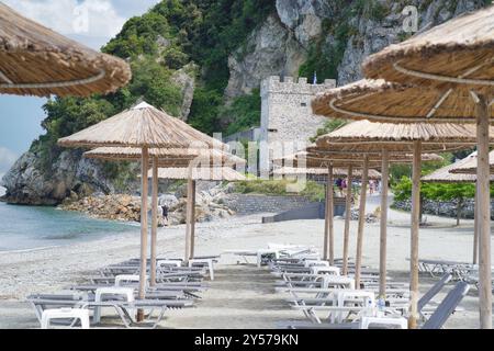 Ein Strand mit Strohschirmen und Liegestühlen an der Ägäis in Griechenland mit der byzantinischen Burg Pantalemon aus dem 13. Jahrhundert im Hinterland Stockfoto