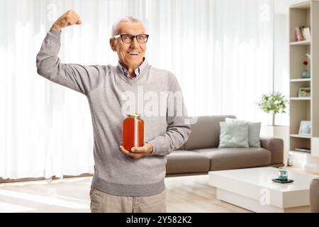 Starker älterer Mann, der ein Honigglas hält und zu Hause Armmuskeln zeigt Stockfoto