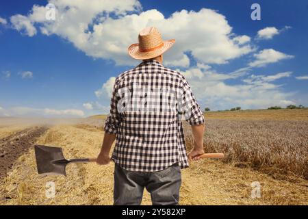 Rückansicht eines Bauern mit Schaufel auf einem Feld Stockfoto