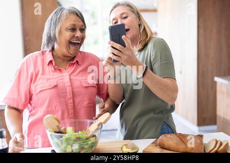 Zu Hause bereiten Seniorenfreunde Salat vor und schauen sich das Smartphone an Stockfoto