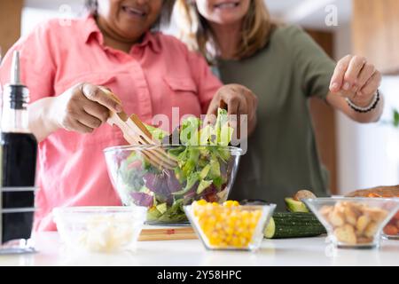 Zu Hause, frischer Salat zubereiten, zwei ältere, multirassische Freundinnen in der Küche Stockfoto