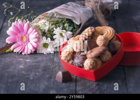 Selektiver Fokus Bild mit einem schönen Blumenstrauß aus Chrysanthemen Die Zustellung der Blumen in alten Zeitung gewickelt und ein unscharfes Kiste voller Süßigkeiten, auf einem schwarzen Holz- Bac Stockfoto