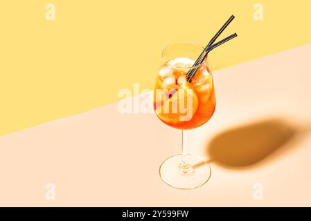 Aperol Spritz Cocktail im Glas mit orangefarbenen Scheiben auf gelbem und pfirsichfarbenem Hintergrund, Kopierraum, trendiges hartes Licht. Köstliches Sommergetränk Aperol Spri Stockfoto