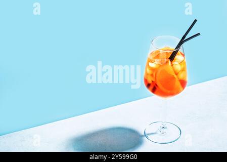 Aperol Spritz Cocktail im Glas mit orangefarbenen Scheiben auf hellblauem Hintergrund, Kopierraum, trendiges hartes Licht. Köstliches Sommergetränk Aperol Spritz Aper Stockfoto