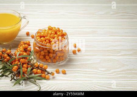 Sanddorn gesunder heißer Tee in der transparenten Glasschale, reife Beeren im Glasgefäß und Zweige mit Blättern auf weißem hölzernen rustikalen Hintergrund, für Haut Stockfoto