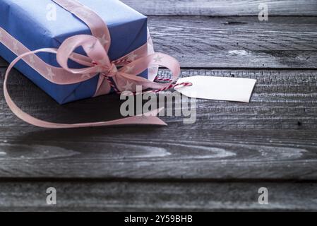 Label tag Geschenk Box in blaues Papier mit Rosa Band auf einem schwarzen Holztisch gebunden gewickelt Stockfoto