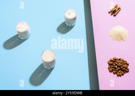 Drei Gläser mit Horchata und Zutaten auf zweifarbigem Hintergrund. Herstellung von Horchata, ein mexikanisches Sommergetränk ohne Alkohol mit Milch, Mandeln und Reis Stockfoto