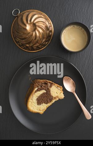 Ein Stück Marmorkuchen auf einem schwarzen Teller mit Kaffee und einer Vintage-Kuchenform Stockfoto