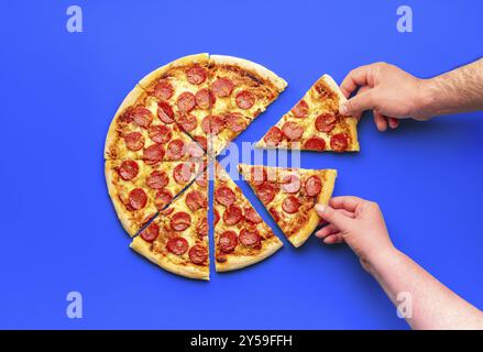 Blick über dem Hotel mit einer geschnittenen Peperoni-Pizza und zwei Händen, die Pizzabäcke schnappen Stockfoto